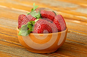 Fresh ripe red strawberries in a clay bowl on an old wooden table,outdoor