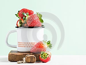 Fresh ripe red strawberries in country style enamel mug on rustic wooden board, pastel light mint background