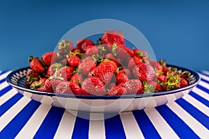 Fresh ripe red strawberries on a huge earthenware dish on a blue-and-white striped table.