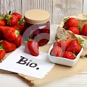 Fresh ripe red strawberries and strawberry jam in a jar, the word BIO on a piece of paper next to it.