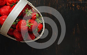Fresh ripe red strawberries in a wicker basket on a brown rustic wooden table
