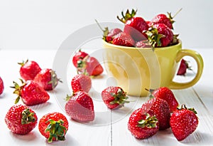 Fresh ripe red strawberries in yellow enamel mug and rough cloth on wooden background