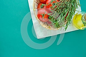 Fresh Ripe Red Tomatoes Rosemary Thyme in Wicker Basket Olive Oil in Bottle on White Napkin Green Background Italian Cuisine