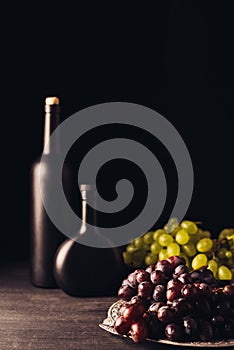 fresh ripe red and white grapes and bottles of wine on wooden table