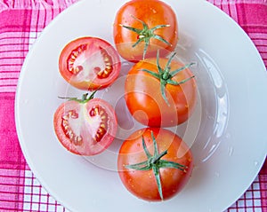 Fresh ripe ripe red tomatoes and cut tomato with water drops and green peduncle on white plate - top view, organic vegetables