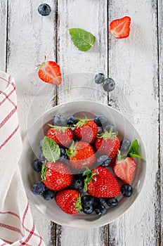 Fresh ripe strawberries and blueberries in a bowl on white wooden rustic background
