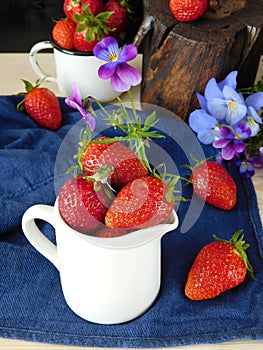 Fresh ripe strawberries in a ceramic jug surrounded by pansies and berries