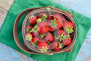 fresh ripe strawberries with green leaves in a wicker basket, on a green napkin, on a rustic wooden table