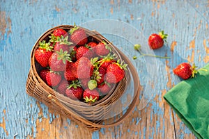 fresh ripe strawberries with green leaves in a wicker basket on a rustic wooden table