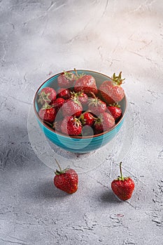 Fresh ripe strawberry fruits in blue bowl, summer vitamin berries on grey stone background