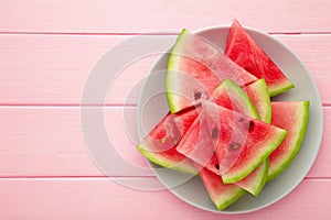 Fresh ripe striped sliced watermelon in the plate on pink wooden background