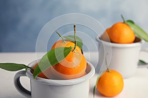 Fresh ripe tangerines with green leaves in cup on table