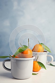 Fresh ripe tangerines with green leaves and mugs on table