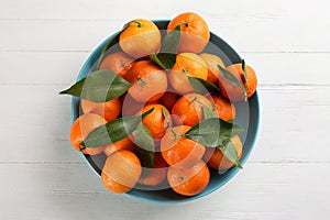 Fresh ripe tangerines with green leaves on white wooden table, top view