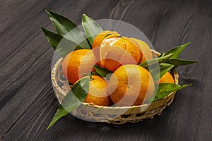 Fresh ripe tangerines with leaves in basket. New Year or Christmas wooden background. Festive good mood concept