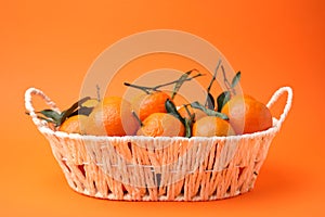 Fresh ripe tangerines and leaves in basket on orange table