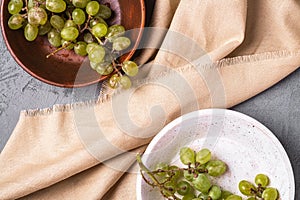 Fresh ripe white grape berries in two wooden bowls on linen tablecloth, stone concrete background