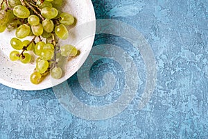 Fresh ripe white grape berries in wooden bowl on blue textured background