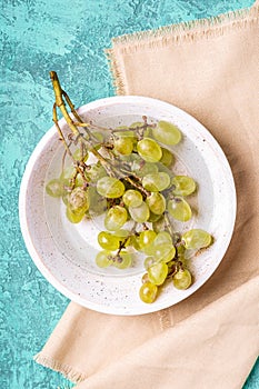 Fresh ripe white grape berries in wooden bowl on linen tablecloth, turquoise textured background