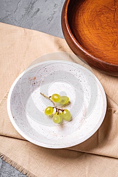 Fresh ripe white grape berries in wooden bowl with plate on linen tablecloth, stone concrete background