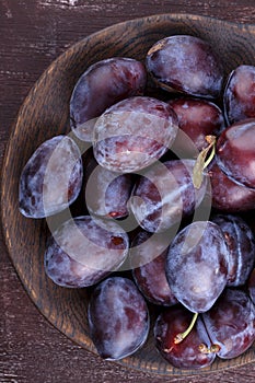 Fresh ripe whole purple damson plums on wooden plate