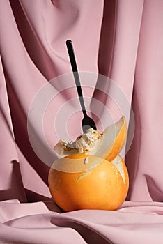 Fresh ripe yellow melon with a black fork on pink drapery,