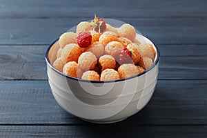 Fresh ripe yellow raspberries in bowl on blue wooden