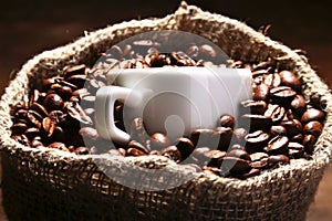 Fresh roasted coffee beans in burlap sack, coffee cup and grinder on dark background.