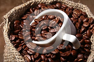 Fresh roasted coffee beans in burlap sack, coffee cup and grinder on dark background.