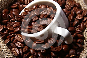 Fresh roasted coffee beans in burlap sack, coffee cup and grinder on dark background.