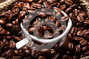 Fresh roasted coffee beans in burlap sack, coffee cup and grinder on dark background.