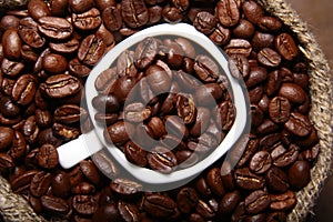 Fresh roasted coffee beans in burlap sack, coffee cup and grinder on dark background.