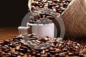 Fresh roasted coffee beans in burlap sack, coffee cup and grinder on dark background.