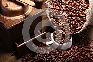 Fresh roasted coffee beans in burlap sack, coffee cup and grinder on dark background.