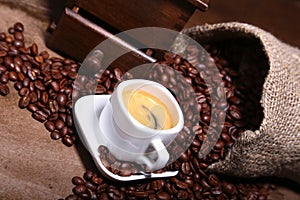 Fresh roasted coffee beans in burlap sack, coffee cup and grinder on dark background.