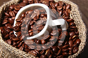 Fresh roasted coffee beans in burlap sack, coffee cup and grinder on dark background.