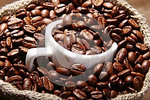 Fresh roasted coffee beans in burlap sack, coffee cup and grinder on dark background.