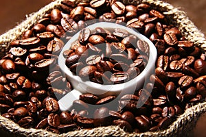 Fresh roasted coffee beans in burlap sack, coffee cup and grinder on dark background.