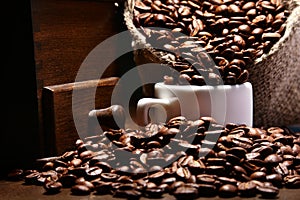 Fresh roasted coffee beans in burlap sack, coffee cup and grinder on dark background.