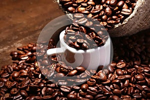 Fresh roasted coffee beans in burlap sack, coffee cup and grinder on dark background.