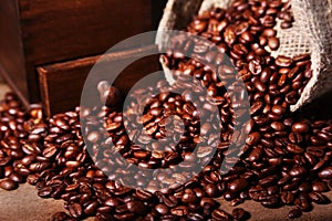 Fresh roasted coffee beans in burlap sack, coffee cup and grinder on dark background.