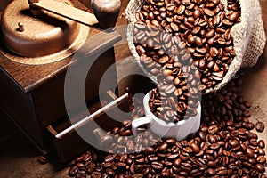 Fresh roasted coffee beans in burlap sack, coffee cup and grinder on dark background.