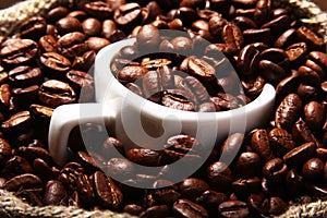 Fresh roasted coffee beans in burlap sack, coffee cup and grinder on dark background.