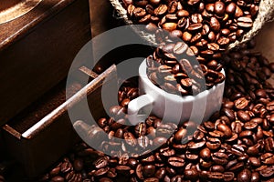 Fresh roasted coffee beans in burlap sack, coffee cup and grinder on dark background.