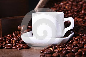 Fresh roasted coffee beans in burlap sack, coffee cup and grinder on dark background.