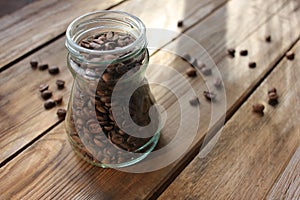 Fresh roasted coffee beans in glass jar on wooden table from above. Scattered coffee beans on wood background