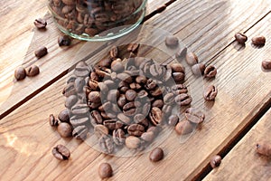 Fresh roasted coffee beans in glass jar on wooden table from above. Scattered coffee beans on wood background