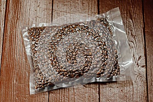 Fresh roasted coffee beans packed in vacuum sealed bag on plank background