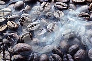 Fresh roasted coffee beans with smoke. Brown roasted coffee beans background. Coffee aroma.