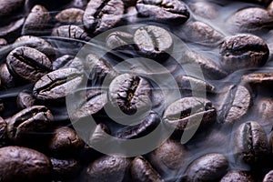 Fresh roasted coffee beans with smoke. Brown roasted coffee beans background. Coffee aroma.